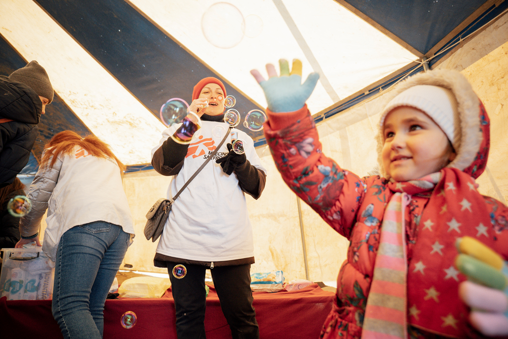 A little girl is playing with bubbles in an MSF operational centre tent.