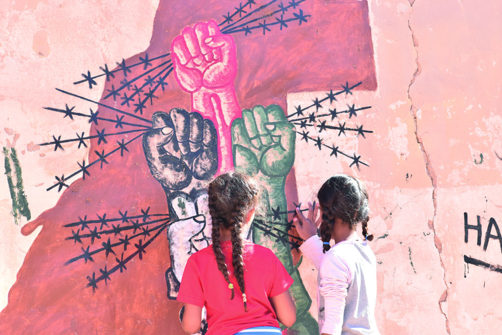 Two girls painting a wall with barbed wire.