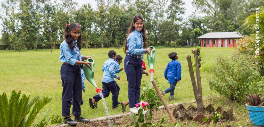 A group of children supported by the terre des hommes foundation are watering plants in a garden.