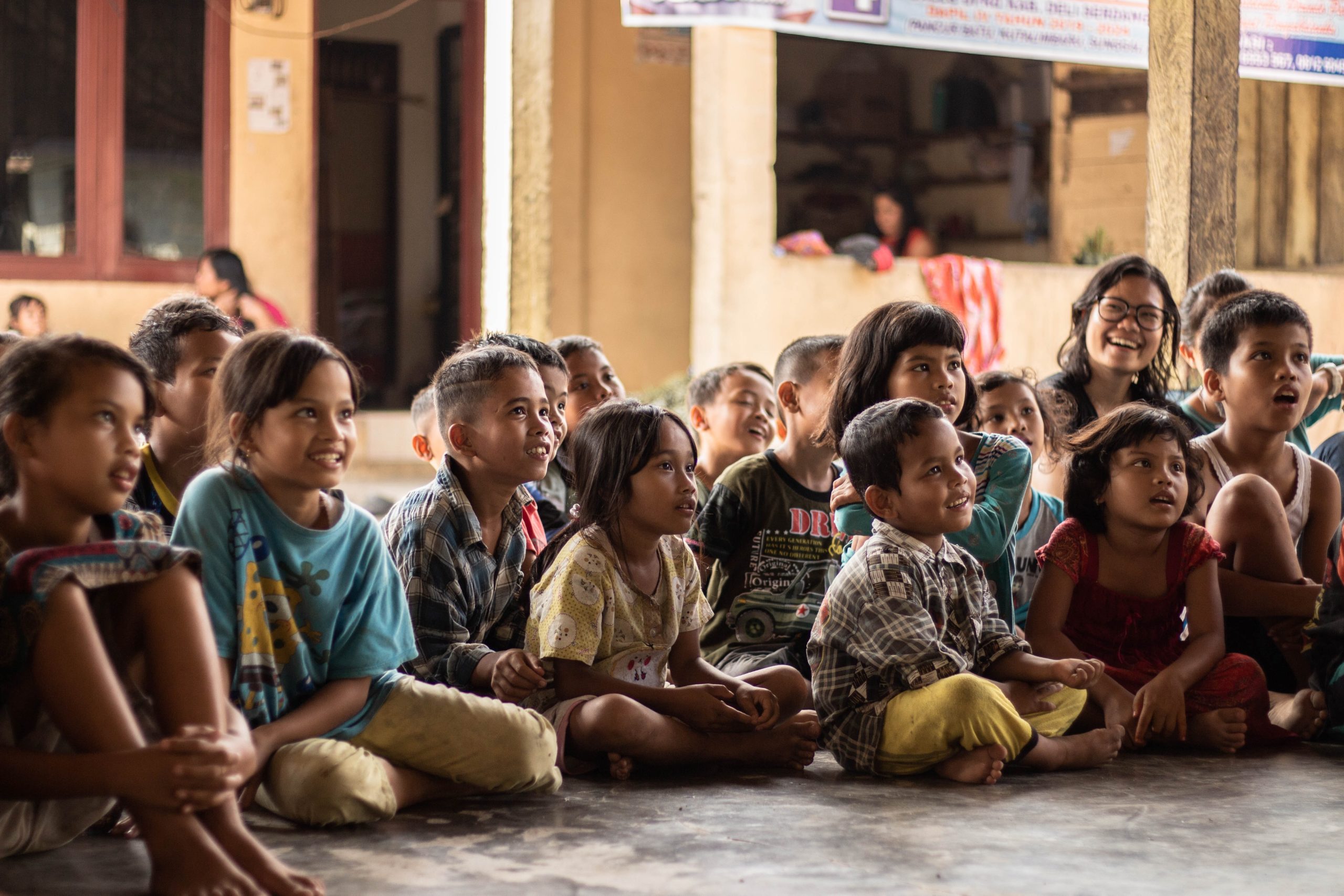 A group of children sitting on the ground in front of a building at an MSF operational centre in Paris.