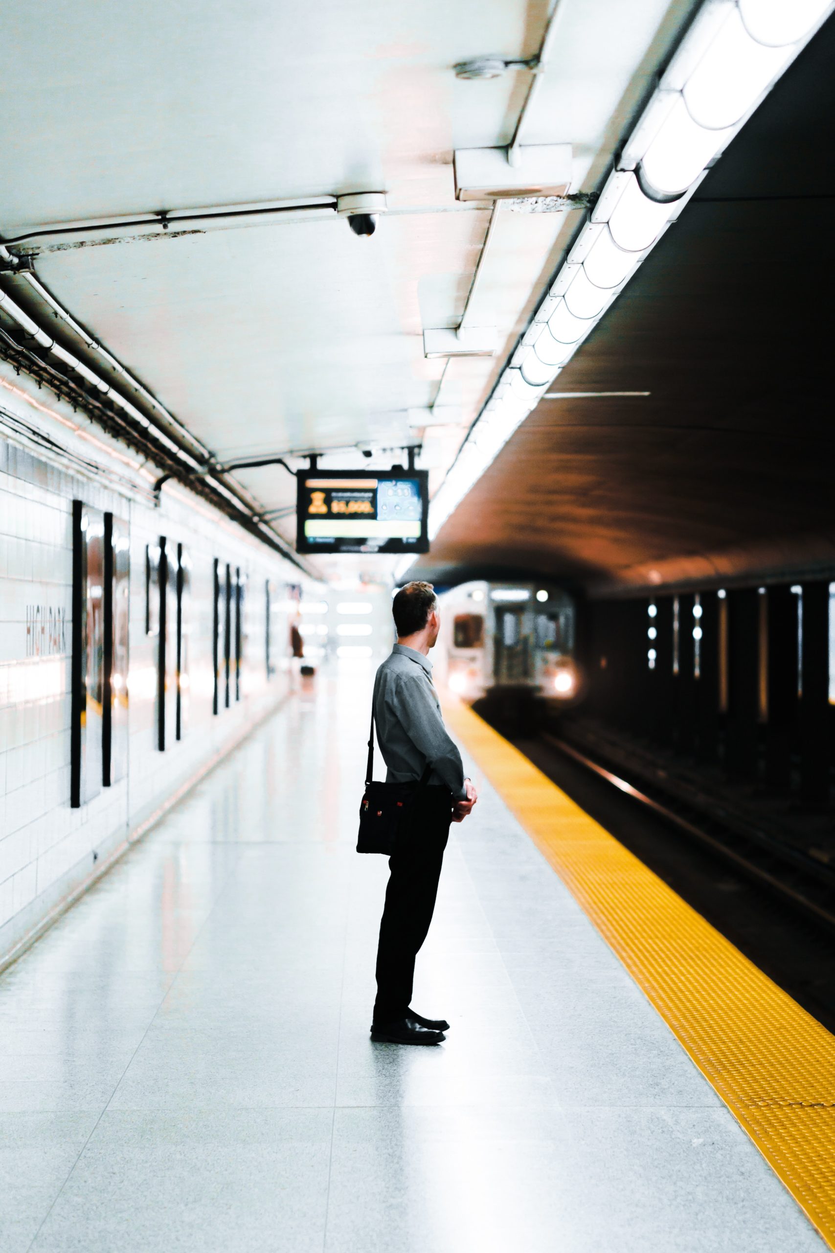 A man commuting, standing on a platform waiting for a train.