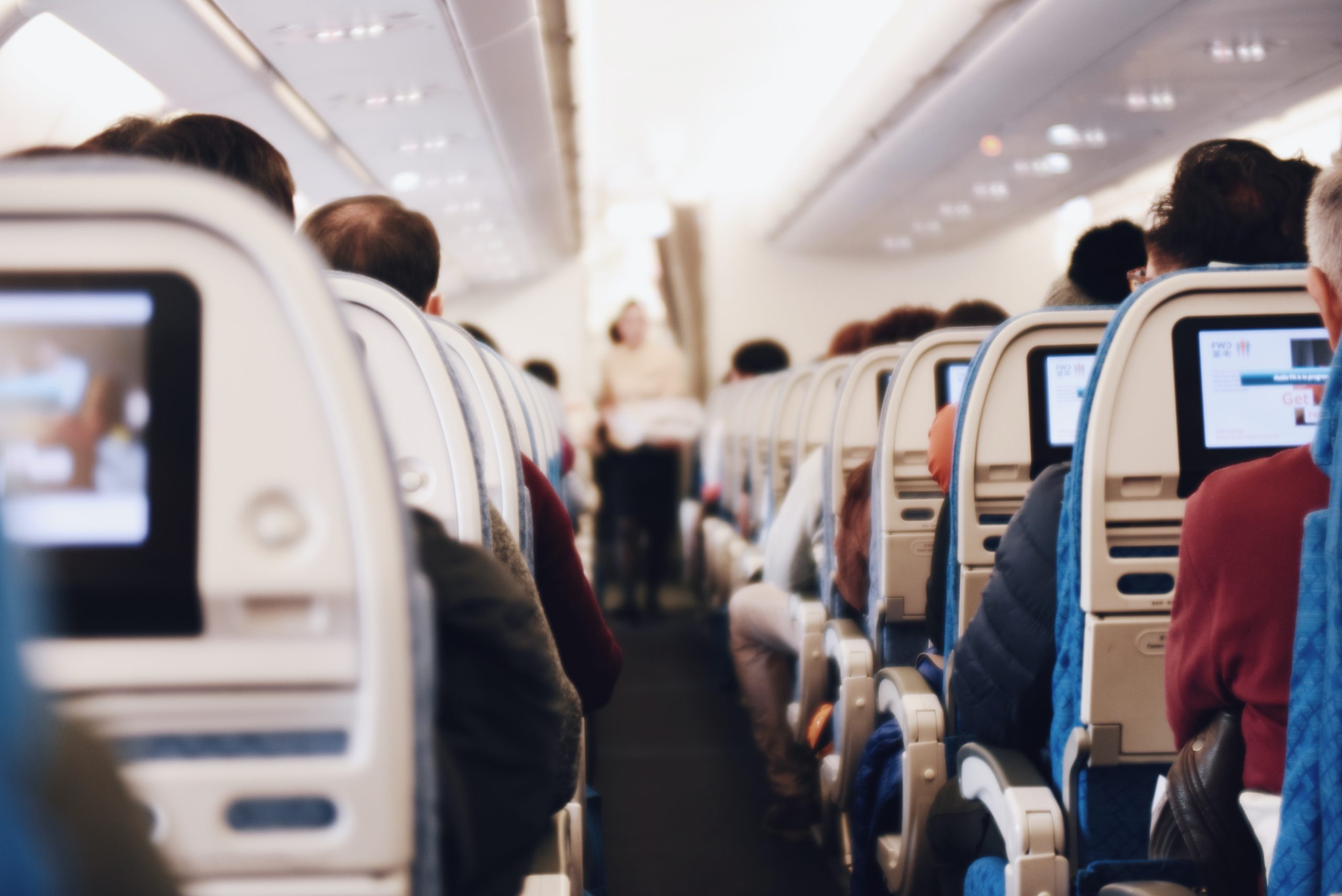 A group of people sitting in an airplane during business travel, watching tvs.