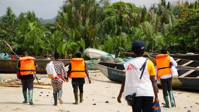 A group of people walking on a beach with boats in the background while considering their published carbon footprints.