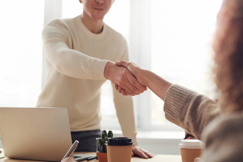 A man shaking hands with a woman in front of a laptop, representing professional collaboration.